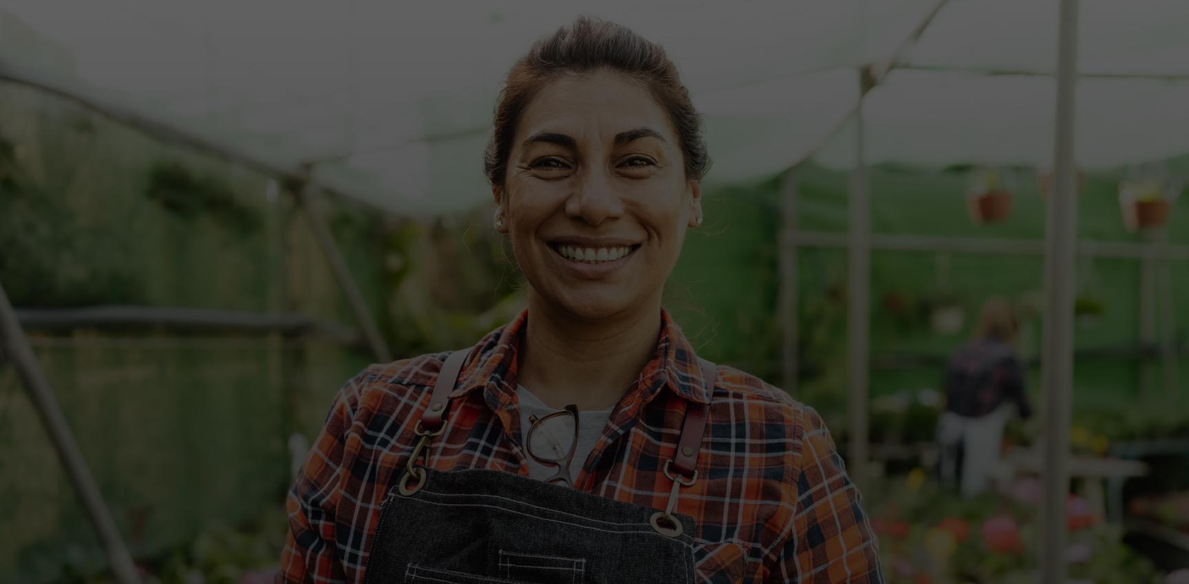 Hispanic woman wearing overalls stands in a greenhouse, Teva Clinical Trials, diversity, research, health equity.